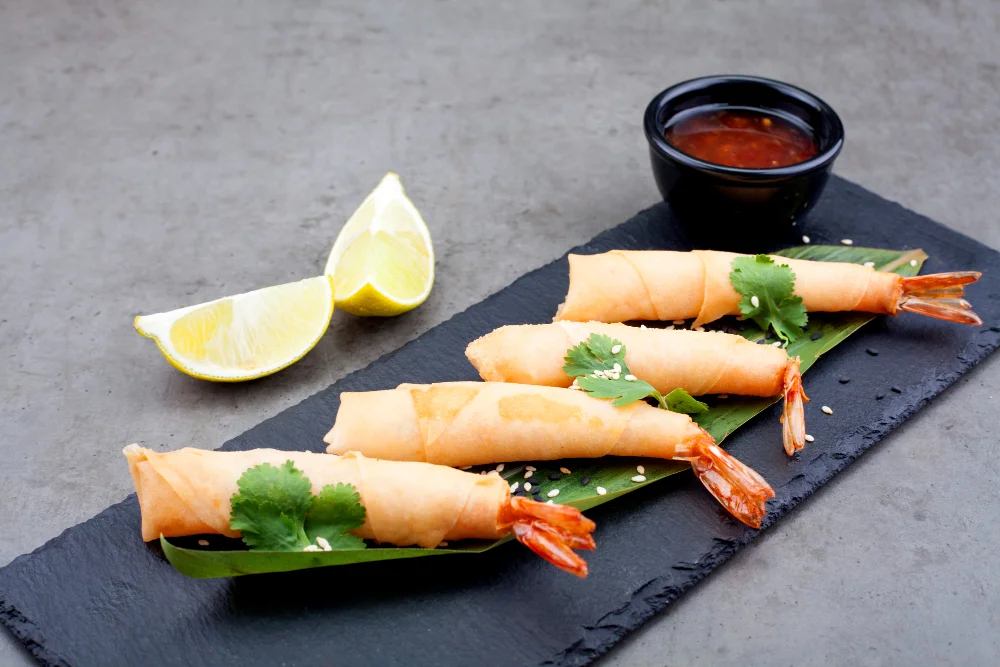 Four prawn spring rolls on a black slate board