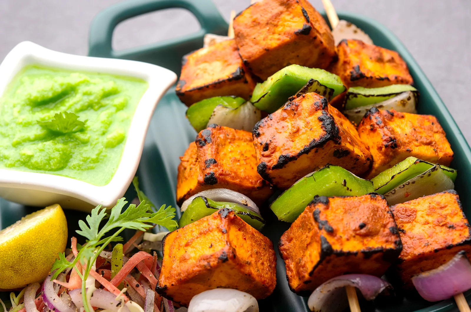 Tandoori Paneer Tikka garnished with fresh cilantro and onion slices, with a wedge of lemon