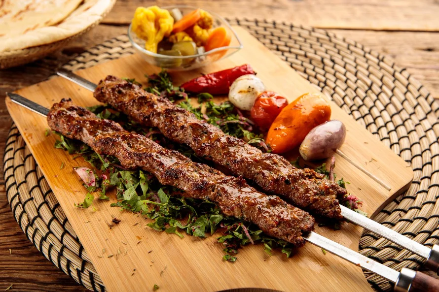 Two grilled seekh kebabs on metal skewers served on a wooden board